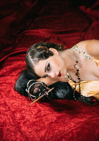 retro look and pinup. Pin up pretty fashion model on red blanket. Girl in yellow dress and fur with mouthpiece. Woman with stylish retro hair, makeup and cigaterre holder.Beauty and vintage fashion.の写真素材