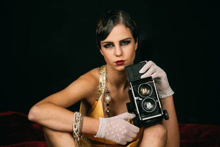 Girl with vintage photo camera. Pin up pretty fashion model photographer. Woman with retro hair, makeup and old camera. beauty, retro look, pinup fashion. media and new technology, journalism.の写真素材