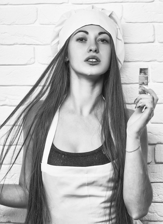 Pretty girl or beautiful woman, cute cook or baker in chef hat and apron keeps metal, star shaped, cookie cutter on white brick wallの写真素材