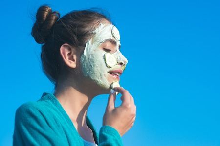 Girl or woman apply cucumber mask on face on blue sky. Beauty, nature, youth, skin care, rejuvenation concept, copy spaceの写真素材