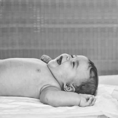 Closeup portrait view of one funny smiling cute little baby boy with blonde hair lying on bed with...