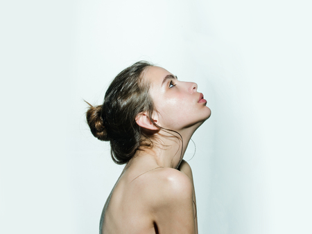 Girl with hair bun, nude shoulders look up on white background. Beauty salon concept. Skin care, health, wellness.の写真素材