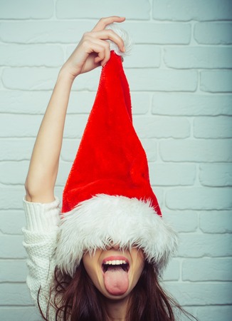 New year girl show tongue. Santa claus girl in red hat. holiday and celebration. Xmas and party. Christmas woman with happy face.の写真素材