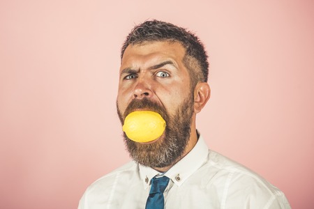 Vegetarian, health and wellbeing. Man with long beard eat lemon. Dieting and fitness. Fruit and healthy organic food. Vitamin citrus at hipster on pink background.の写真素材
