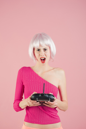 woman in wig hair play with game console and has shouting face on pink background, video gameの写真素材