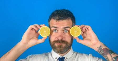 Vegetarian, health and wellbeing. Dieting and fitness. Fruit and healthy organic food. Man with long beard hold lemon. Vitamin citrus at hipster on blue background.の写真素材