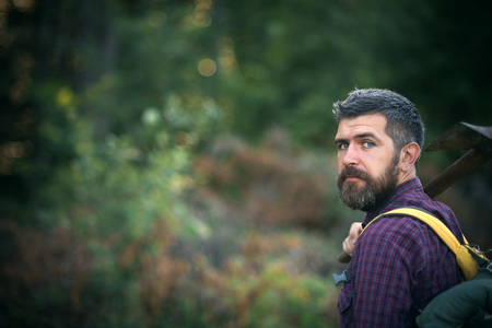 Man hiker hold axe and backpack on summer day on natural landscape, bokeh effect. Logging and chopping concept, copy spaceの写真素材