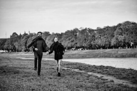 Young couple of pretty girl and bearded man hipster run outdoors in park on autumn day on natural background near waterの写真素材