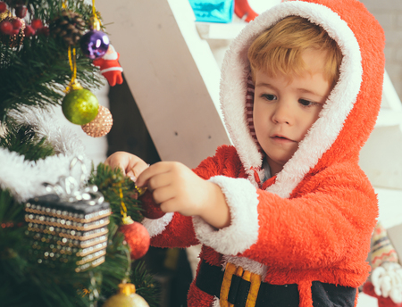 Santa claus kid decorating Christmas tree.. Christmas happy child with gift. Winter holiday and vacation. Xmas party celebration. New year small boy at decoration toy.の写真素材