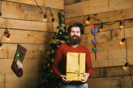 Boxing day and party celebration. Santa claus man with gift pack. Christmas man with beard on happy face at present box. Winter holiday and xmas. New year guy at Christmas tree with garland.の写真素材