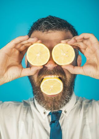 Dieting and fitness. Vitamin citrus at hipster on blue background. Man with long beard eat lemon. Vegetarian, health and wellbeing. Fruit and healthy organic food.の写真素材