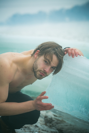 Winter holiday and activity. Cracked ice at Hercules guy in Christmas. Power and strength of man with frozen hummock. Cold weather and ice age. Man with bare muscular chest hold big ice block.の写真素材