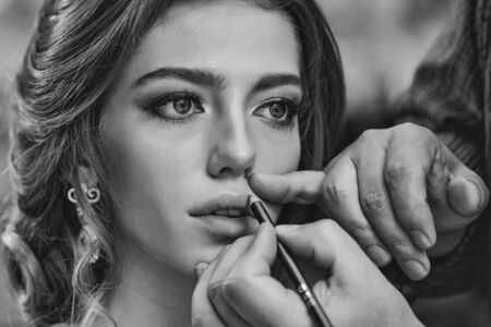 Guy stylist doing makeup beautiful woman in beauty salon with wavy hairstyleの写真素材