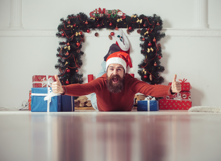 Christmas man with beard on happy face at present box. New year guy at Christmas decoration fireplace. Santa claus man with gift pack. Winter holiday and xmas. Boxing day and party celebration.の写真素材