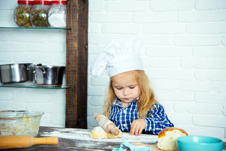 Child cook in chef hat rolling dough with wooden pin on kitchen table. Homemade cooking and baking. Playing and learning. Happy childhood concept.の写真素材