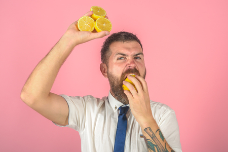 Vegetarian, health and wellbeing. Fruit and healthy organic food. Vitamin citrus at hipster on pink background. Man with long beard eat lemon. Dieting and fitness.の写真素材