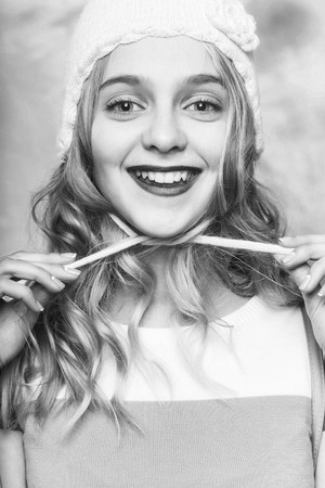 Happy pretty girl or beautiful woman with big eyes, red lips and blond curly hair in green ties cute knitted blue, beanie, hat on head on pink backgroundの写真素材