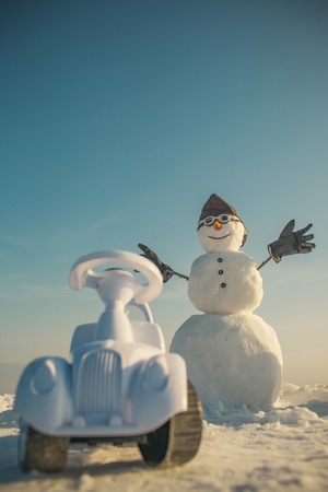 Christmas and transportation. Happy holiday celebration. Snowman in winter with toy car, travel and vaction. Xmas or christmas decoration, aviation. New year snowman in pilot hat and glasses.の写真素材