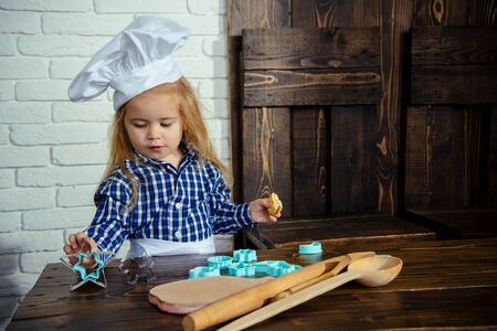 Playing and learning. Boy cook in chef hat in kitchen. Homemade cooking and baking. Child using spoon, rolling pin and cookie cutters on table. Happy childhood concept.の写真素材