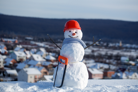 Happy holiday and celebration. New year snowman from snow with saw. Snowman builder in winter in helmet. Building and repair work. Christmas or xmas decoration.の写真素材