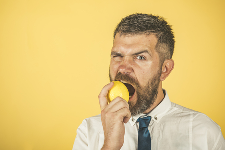 Vegetarian, health and wellbeing. Dieting and fitness. Vitamin citrus at hipster on yellow background. Man with long beard eat lemon. Fruit and healthy organic food, copy spaceの写真素材