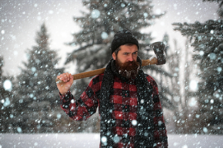 new year christmas snow concept Christmas hipster lumberjack with ax in wood.. Man with beard in winter forest with snow hold axe. Winter holiday and celebration. New year man in snowy cold forest.の写真素材