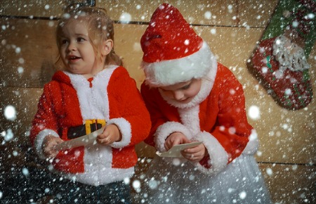 christmas new year snow concept New year small girl and boy, happiness. Winter holiday and vacation. Santa claus kid at Christmas tree. Xmas celebration, childhood Christmas happy children in red hat.の写真素材