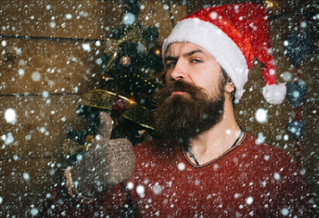 christmas new year snow concept thumb up gesture and party celebration. Winter holiday and xmas. Santa claus man on wooden background. Christmas man with beard on serious face. New year guyの写真素材