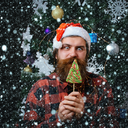 christmas new year snow concept Party celebration and blowjob. santa claus man in hat at decoration. Christmas man with beard on happy face and lollipop. Winter holiday xmas. New year guy lick candyの写真素材