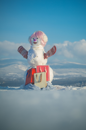 New year snowman with shopping bag. Snowman girl in winter pink wig hair with bag. Happy holiday celebration. Xmas or christmas party, present pack. Christmas and winter fashion.の写真素材
