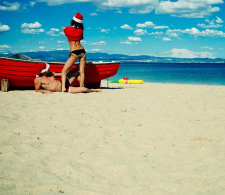 Christmas couple in red at beach boat. Couple in love of happy man and woman, travel. New year girl and guy as santa. Xmas party celebration. Winter holiday and vacation, copy spaceの写真素材