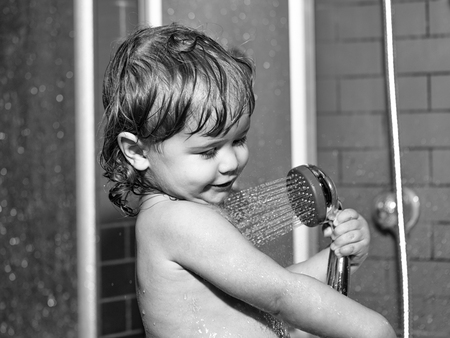 Cute happy smiling funny undressed boy child with blonde curly wet hair taking shower in bath with...