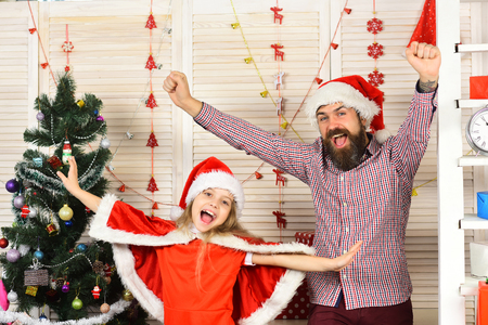 Happy family celebrate new year and Christmas. Father and child with raised hands. Father and daughter in santa hat at Christmas tree. Xmas party celebration. Winter holiday. New year greeting.の写真素材