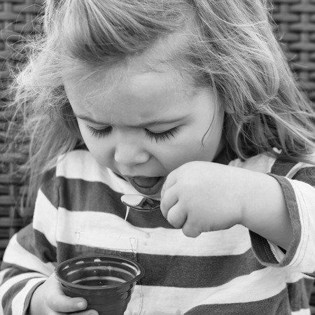 Cute baby boy eating tasty ice cream, small, little child with long, blond hair in blue, striped clothes holds frozen pink dessert in cup, on chair in outdoor cafe sunny day. Idyllic summer vacationの写真素材