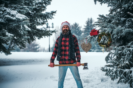 New year man in snowy cold forest with gift box. xmas wanderlust, hiking and travel. Christmas hipster lumberjack with ax in wood. Winter holiday celebration. Man with beard in winter forest with axe.の写真素材