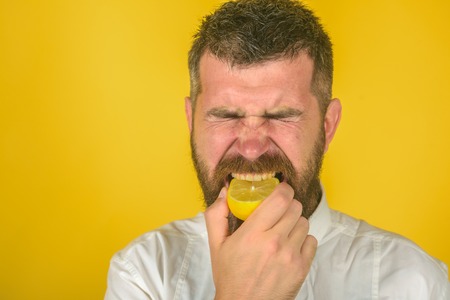Fruit and healthy organic food. Man with long beard eat lemon. Vitamin citrus at hipster on yellow background. Dieting and fitness. Vegetarian, health and wellbeing, copy spaceの写真素材