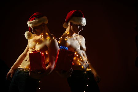 New year strip and gifts for adults. Call boys or sexy athlete men at xmas. Christmas party and sex games. Twins santa with muscular body in garland. Young men in santa costume, present for girls.の写真素材