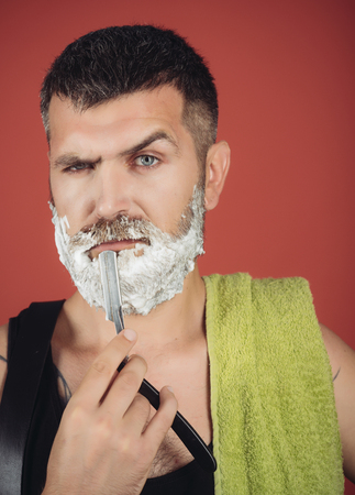 Fashion and beauty, innovation. Barber and hairdresser. Serious hipster in barbershop, new technology. Man cut beard and mustache with razor and shaving gel. Haircut of bearded man, archaism.の写真素材