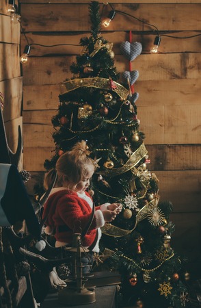 Santa claus kid at Christmas tree. Christmas happy child read wish letter. New year small boy with paper. Winter holiday and vacation. Xmas party celebration.の写真素材