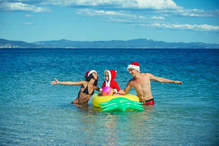 Santa child, parents at Christmas. Christmas happy family on pineapple mattress in water. Xmas party celebration, fathers and mothers day. Winter holiday vacation. New year man, girl with small boy.の写真素材