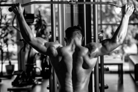 Handsome young man with sexy muscular wet body and bare back training with heavy exercise equipment in gymの写真素材