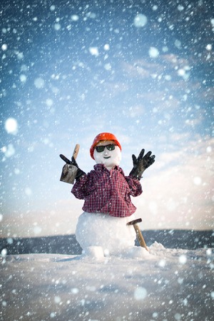 new year christmas snow concept Building and repair work. Snowman builder in winter in helmet. Happy holiday and celebration. Christmas or xmas decoration. New year snowman from snow with hammerの写真素材