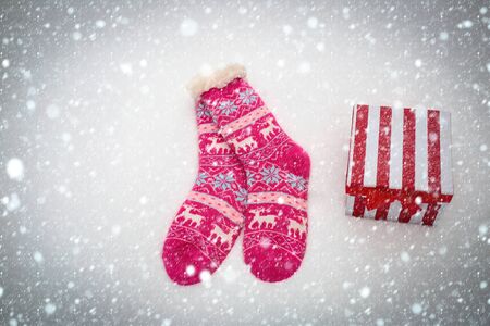 new year christmas snow concept Pair of socks and gift box on snowy background. Knitted socks with ornament and present pack on white snow. Christmas and new year surprise. Winter holidays celebrationの写真素材