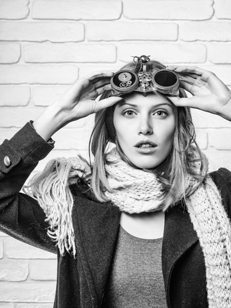 Pretty girl young cute beautiful woman or watchmaker with watch mechanical metallic gears and cogwheels on red hair on white brick wallの写真素材