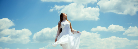Girl or woman with long hair in white dress enjoy sunny summer day on cloudy blue sky. Freedom, future conceptの写真素材