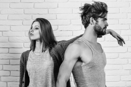 Young couple of handsome man or muscular macho in grey undershirt with pretty cute girl or beautiful woman in knitted coat on white brick backgroundの写真素材