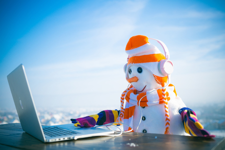 Snowman in winter with laptop, headset and tea cup. Xmas or christmas decoration, audio book. Happy holiday celebration, new technology. New year snowman in hat. Christmas and hot wine..の写真素材