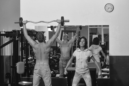 couple of pretty woman or cute girl and handsome guy or macho man with muscular torso and sexy body training in sport gym with barbell and dumbbells at trainer of weight liftingの写真素材