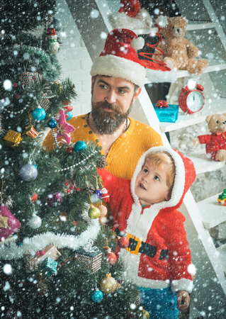 Santa claus kid and bearded man at Christmas tree. Christmas happy child and father. New year small boy son and man with toy. Winter holiday and vacation. Xmas party celebration, fathers day.の写真素材