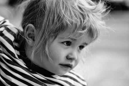 Cute baby boy child with curly blond hair and brown eyes in striped shirt outdoors on summer dayの写真素材